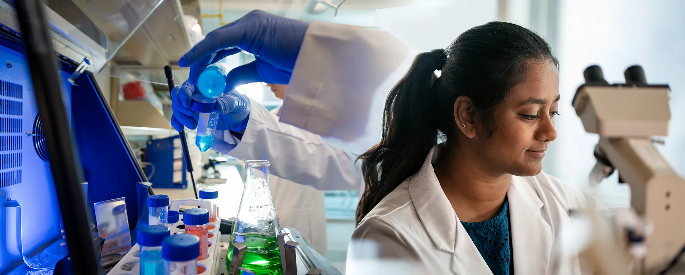 a dual image with gloved hands filling a tube beside a computer on the left side and next to it a female in a lab coat with a microscope in the background